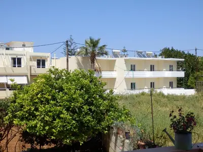 a white building with a palm tree in front of it at Charisma Apartment in Plataniás
