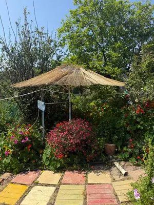 a garden with a straw umbrella and some flowers at Modern 1-bedroom with BBQ & Roof Garden near Beach in Stalos