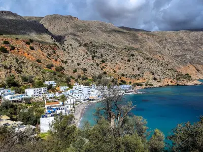 a view of a beach with blue water and white buildings at Kyma in Loutro
