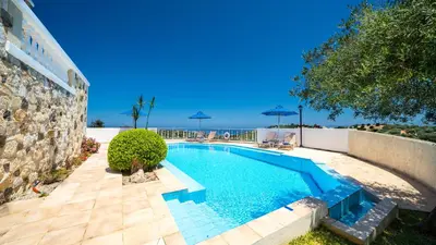a swimming pool with chairs and umbrellas next to a building at Ilios Village in Stalos