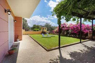 a courtyard with a garden with two chairs and pink flowers at Maria's Garden in Galatás