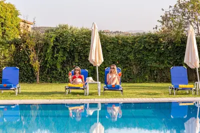 two women sitting in chairs next to a swimming pool at Alonia Hotel Apartments in Kolymvari