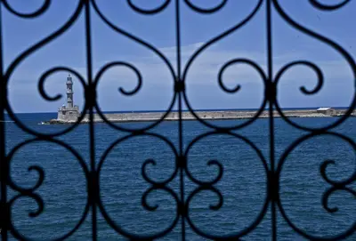 a view of a lighthouse through a iron fence at Mosaic Venetian Harbour Suites in Chania Town