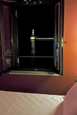 a room with a window with a lighthouse in the water at Mosaic Venetian Harbour Suites in Chania Town