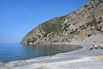 a beach with chairs and umbrellas next to the water at Calypso in Agia Roumeli