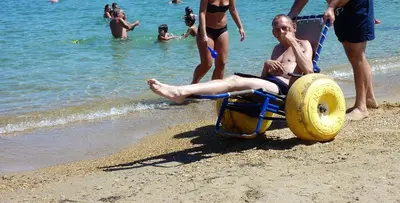 a man laying on a beach in a wheelbarrow at ERIA RESORT for people with special abilities in Maleme