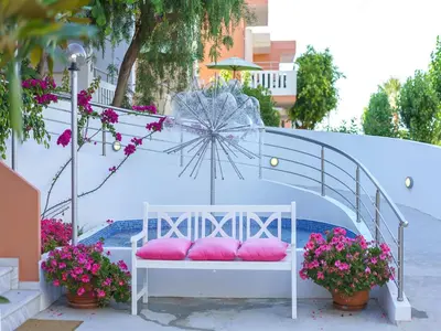 a white bench with pink pillows on it next to flowers at Sonio Beach - Que Bella Collection in Plataniás