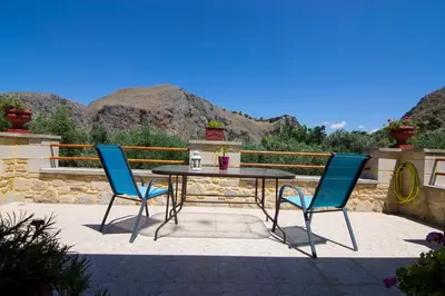 a table and chairs on a patio with mountains in the background at Mansion Rokka in Kissamos