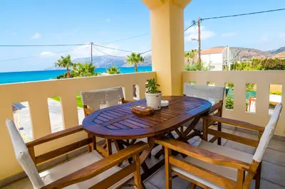 a wooden table and chairs on a balcony with the ocean at Thalassa Apartments in Kissamos