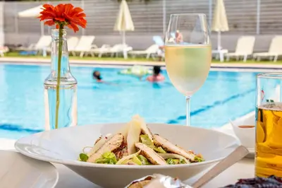a plate of food and a glass of wine next to a pool at Dimitra & Evdokia Hotel in Agia Marina Nea Kydonias