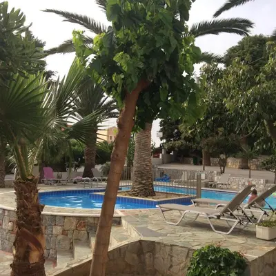 a resort pool with palm trees and a chair at Maria Suites in Plataniás