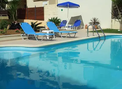 a swimming pool with blue chairs and an umbrella at Nicolas Studios & Apartments in Agia Marina Nea Kydonias