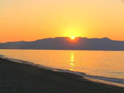 a sunset on the beach with mountains in the background at Katerina Seaside Studios in Plataniás