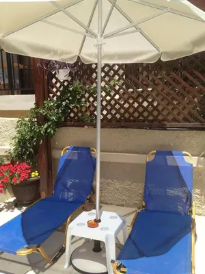two blue chairs and an umbrella on a patio at Angelica Studios and Apartments in Agia Marina Nea Kydonias