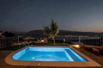 a swimming pool at night with a view of the water at Istros Villas - with Pools, BBQ & Heated Spa Whirlpools, By ThinkVilla in Korakiaí
