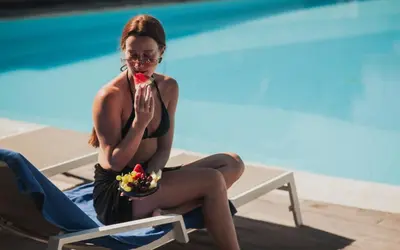 a woman sitting on a chair next to a swimming pool at Royal Sun in Chania Town