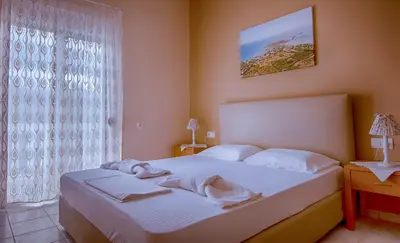 a bedroom with a bed with white sheets and a window at Oriental Bay in Palaiochóra