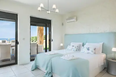 a white bedroom with two beds and a balcony at Villa Emilia front sea in Kalathas