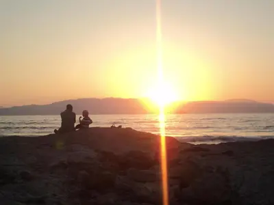 a man and a child sitting on the beach watching the sunset at Thodorou Villa in Agia Marina Nea Kydonias