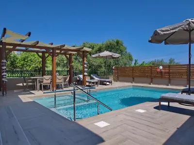 a swimming pool with tables and chairs and an umbrella at Villa Andreas in Kamisianá