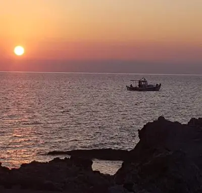 a boat in the ocean with the sunset in the background at Haris Studios in Palaiochóra
