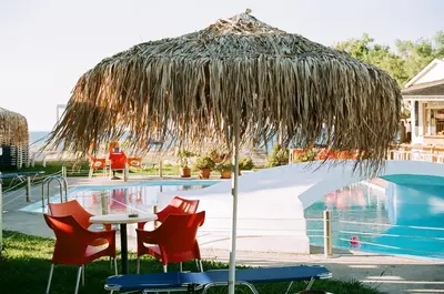 a table and chairs under a straw umbrella next to a pool at Hippokratis Apartments in Gerani Chanion