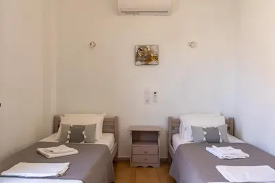 two twin beds in a room with a table at Giannis Rooms in Agia Roumeli