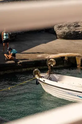 a boat tied to a dock with a person sitting on the water at Giannis Rooms in Agia Roumeli