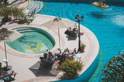 a group of people sitting around a swimming pool at Dionyssos Village in Kato Daratso