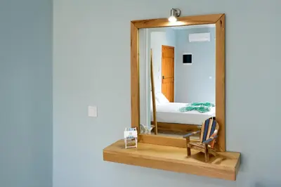 a mirror on a wooden shelf with a chair and a bed at Katerina Apartments in Kato Daratso