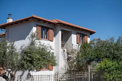a white house with brown windows and trees at Andromia Studios & Apartments in Agia Marina Nea Kydonias