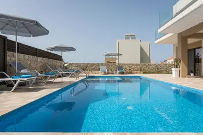 a pool with chairs and umbrellas next to a building at Villa Kambos Platanias in Plataniás