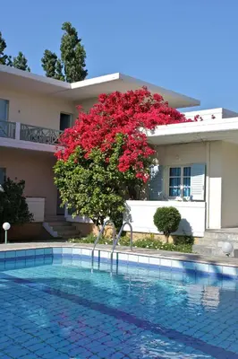 a house with a red tree next to a swimming pool at Cormoranos Apartments Rooms Eco Green in Kissamos