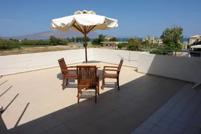 a table and chairs with an umbrella on a roof at Cormoranos Apartments Rooms Eco Green in Kissamos