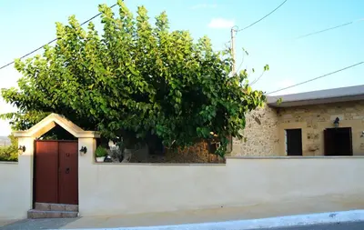 a house with a tree behind a white fence at Kamara Stone House in Kissamos