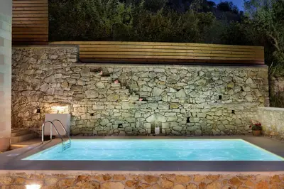 a swimming pool in front of a stone wall at Olga's Filoxenia - Villa Aladanos-private pool and heated jacuzzi in Makhairoí