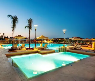 a pool with chairs and palm trees in a resort at Porto Platanias Village Resort in Plataniás