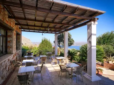 a patio with tables and chairs under a wooden pergola at Areti Aparthotel in Áptera