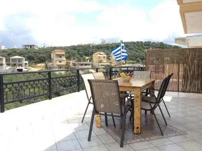 a wooden table with chairs and a flag on a balcony at Anatoli View in Agia Marina Nea Kydonias