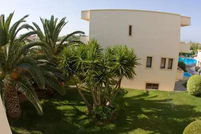 a building with palm trees in front of a yard at Olga Suites in Maleme