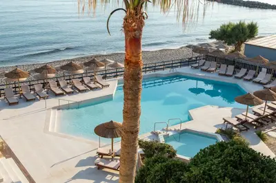 a swimming pool with chairs and a palm tree at Hotel Haris on the beach in Agia Marina Nea Kydonias