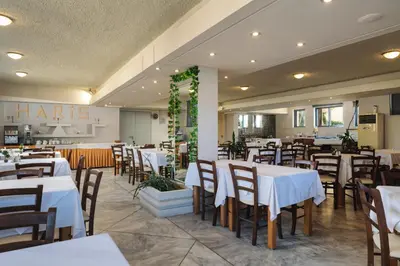 a dining room with white tables and chairs at Hotel Haris on the beach in Agia Marina Nea Kydonias