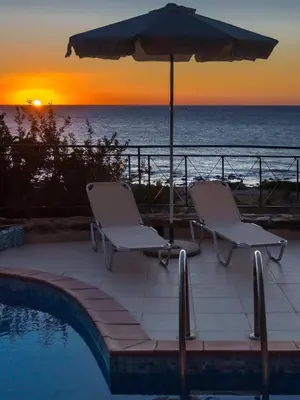 two chairs and an umbrella next to a swimming pool with the ocean at Meliti Sunset View & Private Pool Villa 20 min from Elafonissi in Livadia