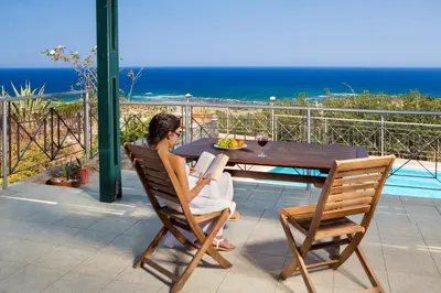 a woman sitting at a table reading a book at Villa Livadia with Pool, close to Elafonissi famous Beach in Livadia
