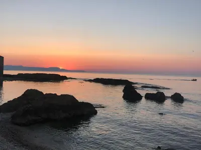 a sunset over the ocean with rocks in the water at Microcosmos Halepas in Chania Town