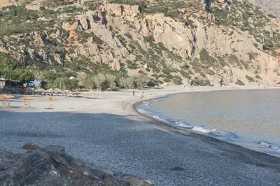 a beach with people walking on the sand and a mountain at Arhondiko Luxury House in Sougia