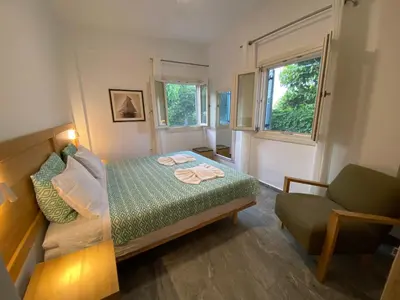 a bedroom with a bed and a chair and a window at Chrisi Holiday Home - 500 sqm Private Gardens & Nature View - 300m by the sea in Almirida