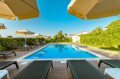 a swimming pool with chairs and umbrellas on a patio at Koulouris Apartments & Studios in Kalyves