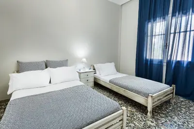 a bedroom with two beds and a window with blue curtains at Anemelia in Chania Town