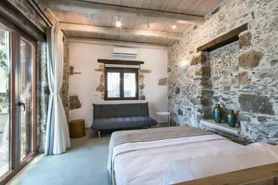 a bedroom with a bed and a stone wall at Stairs Homes & Suites in Kamária